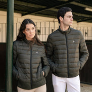 Two people wearing matching green puffer jackets and white pants standing in an equestrian setting.