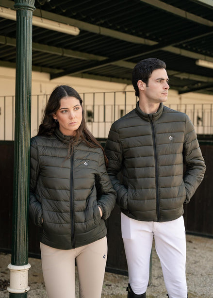 Two people wearing matching green puffer jackets and white pants standing in an equestrian setting.