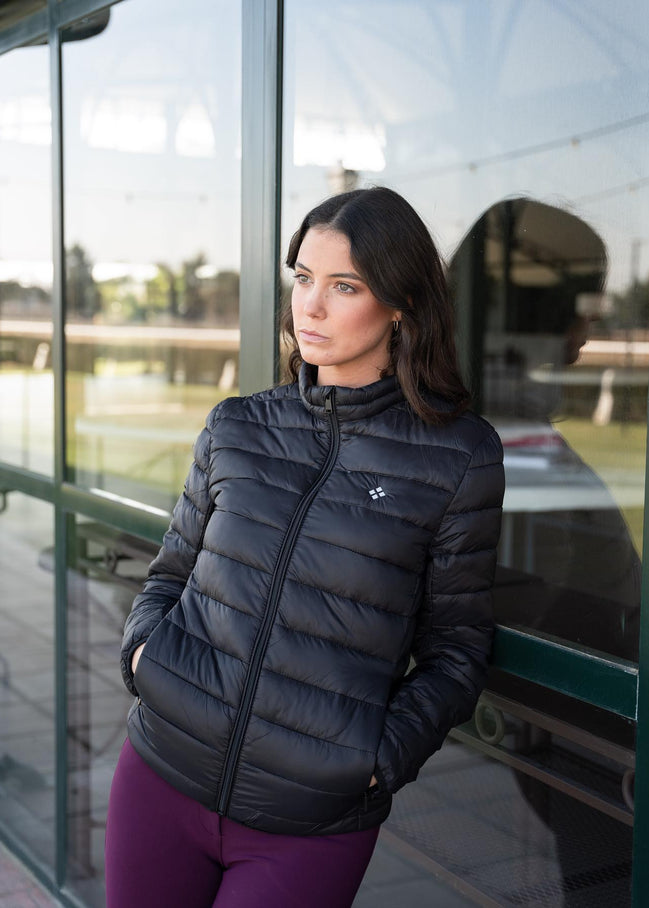 Woman wearing a black puffer jacket standing by a glass door.