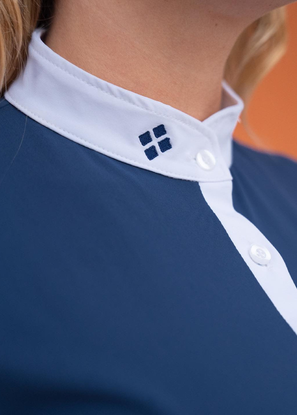 Close-up of a blue shirt with white trim and a logo on an orange background