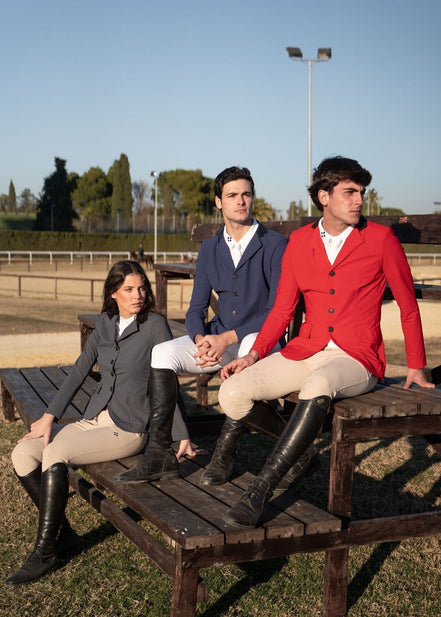Three people in equestrian attire sitting on a wooden bench at an outdoor setting.