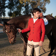 Man in a red jacket standing next to a horse in an outdoor setting