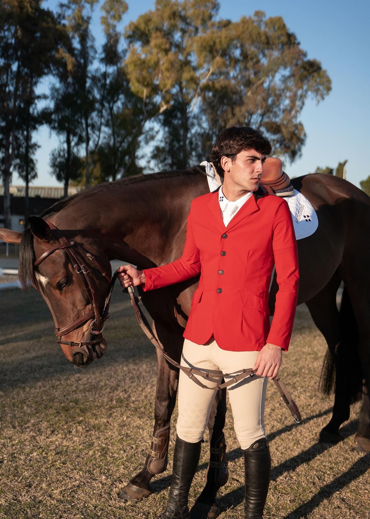 Man in a red jacket standing next to a horse in an outdoor setting