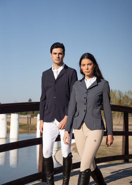 Two people in equestrian attire standing on a bridge with a clear blue sky.