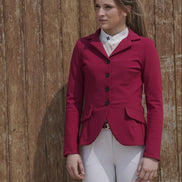 Woman wearing a red equestrian jacket and white pants against a wooden background