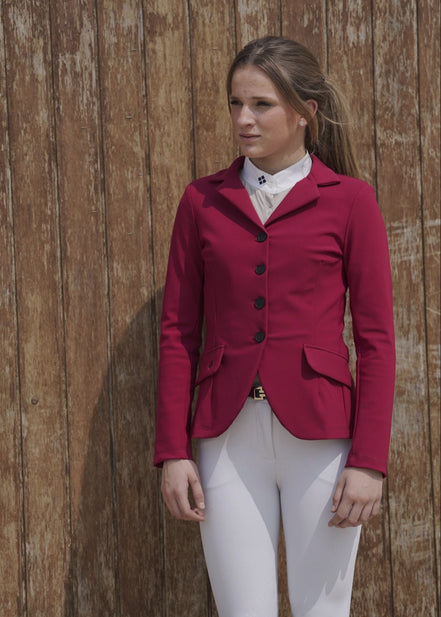 Woman wearing a red equestrian jacket and white pants against a wooden background