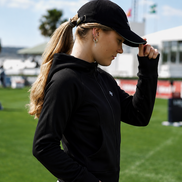 Person wearing a black cap and black jacket on a sports field