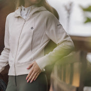 Woman wearing a beige jacket with a brand logo, standing outdoors.