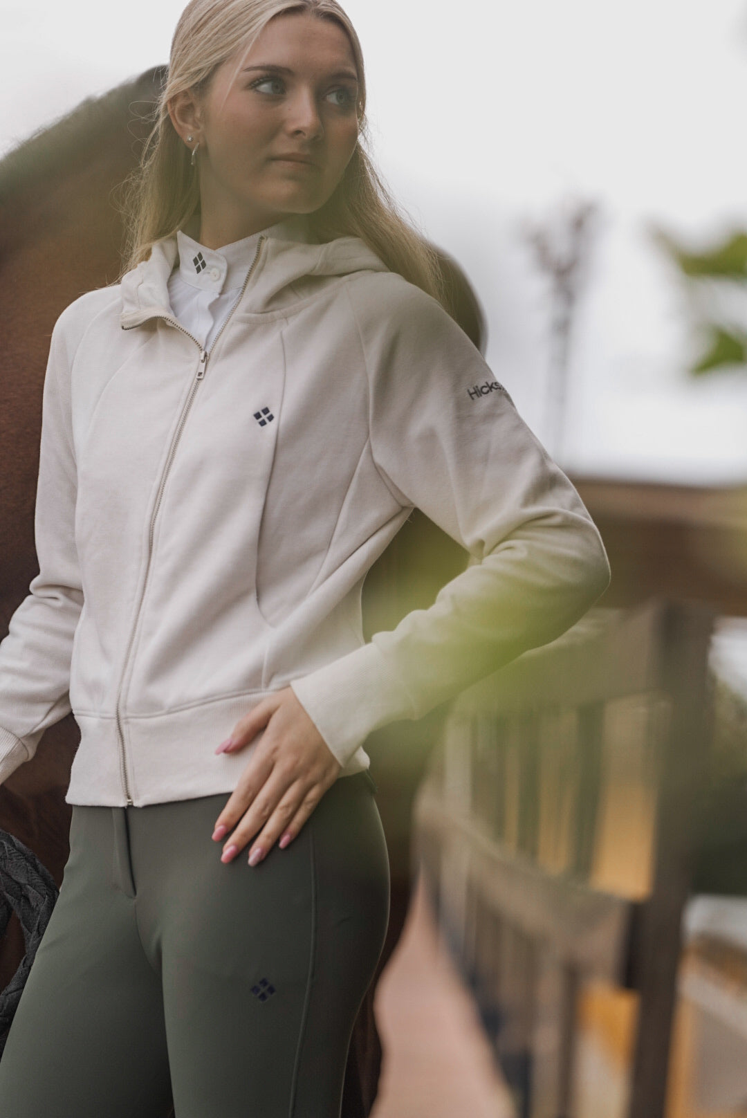 Woman wearing a beige jacket with a brand logo, standing outdoors.