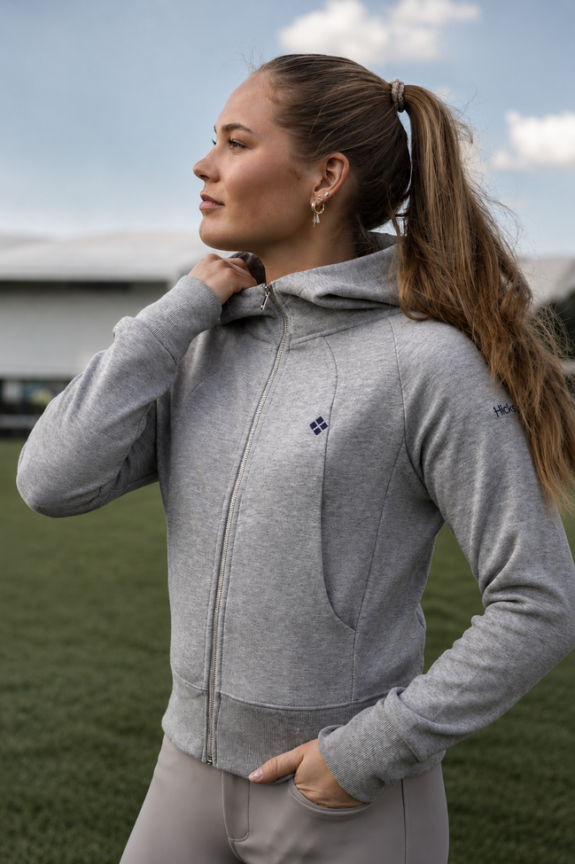 Woman wearing a gray hoodie with a brand logo outdoors