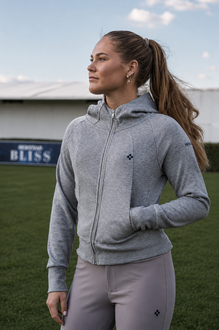 Woman wearing a gray hoodie and light purple pants on a sports field with a blurred background