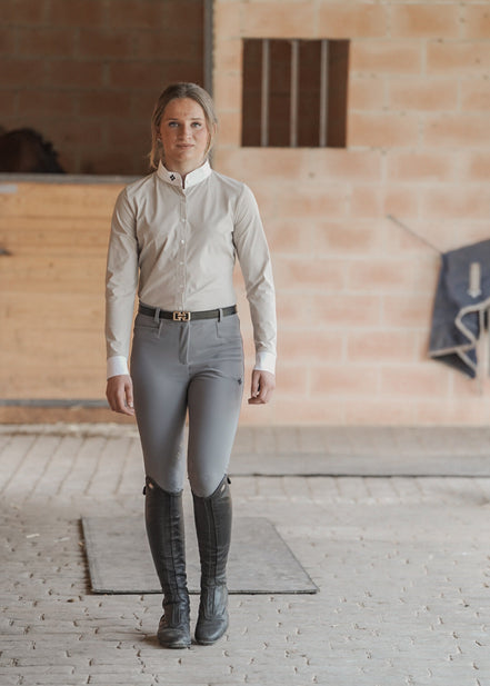 Woman in equestrian attire standing in a stable.