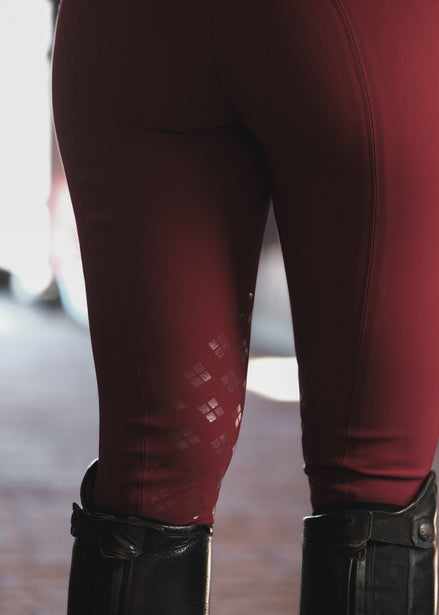 Maroon leggings with a subtle pattern worn with black boots on a blurred background