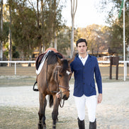 Man in equestrian attire standing next to a horse in an outdoor setting