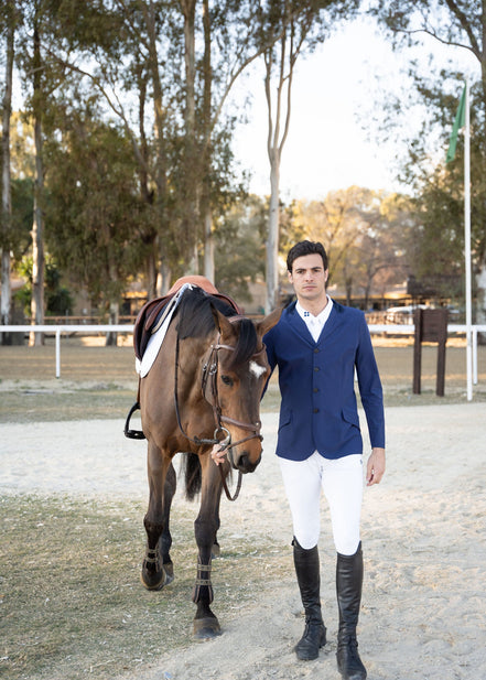 Man in equestrian attire standing next to a horse in an outdoor setting