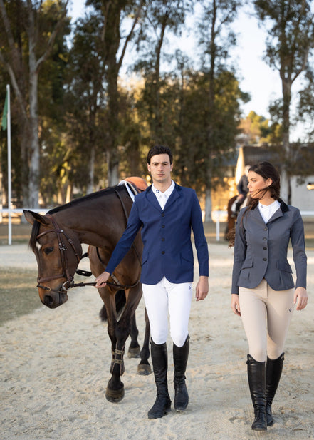Two equestrian riders in formal riding attire walking with a horse on a gravel path.