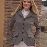 Woman wearing a gray equestrian jacket and white pants standing against a brick wall.