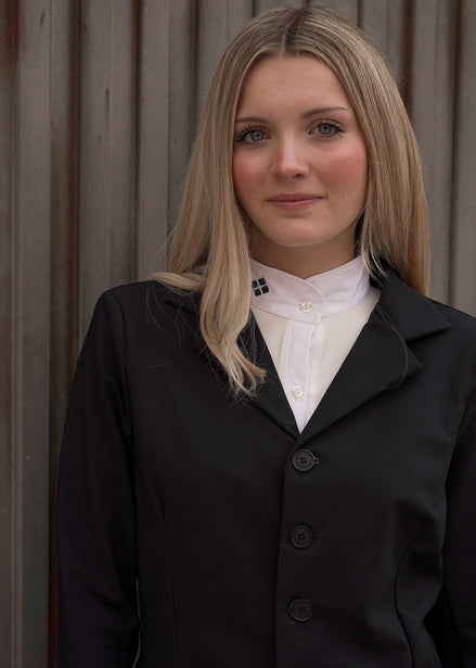 Woman wearing a black coat over a white shirt against a neutral background