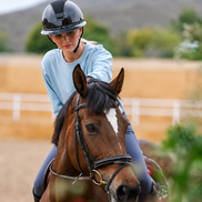 Woman riding a horse in an outdoor setting with mountains in the background