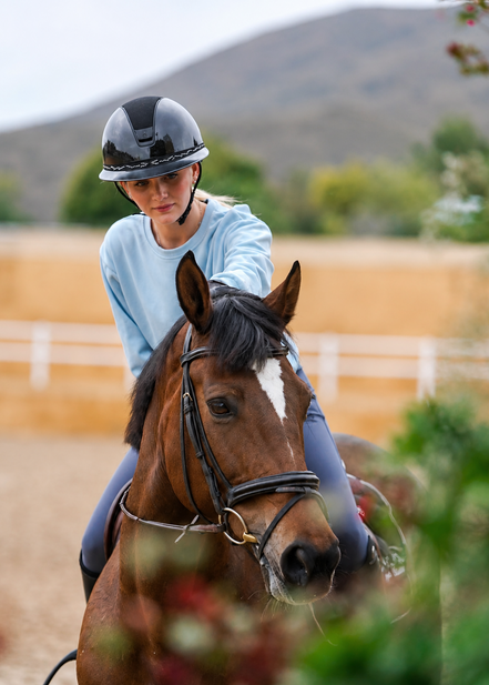 Woman riding a horse in an outdoor setting with mountains in the background