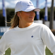 Woman wearing a white cap and long-sleeve shirt with a logo, standing outdoors.