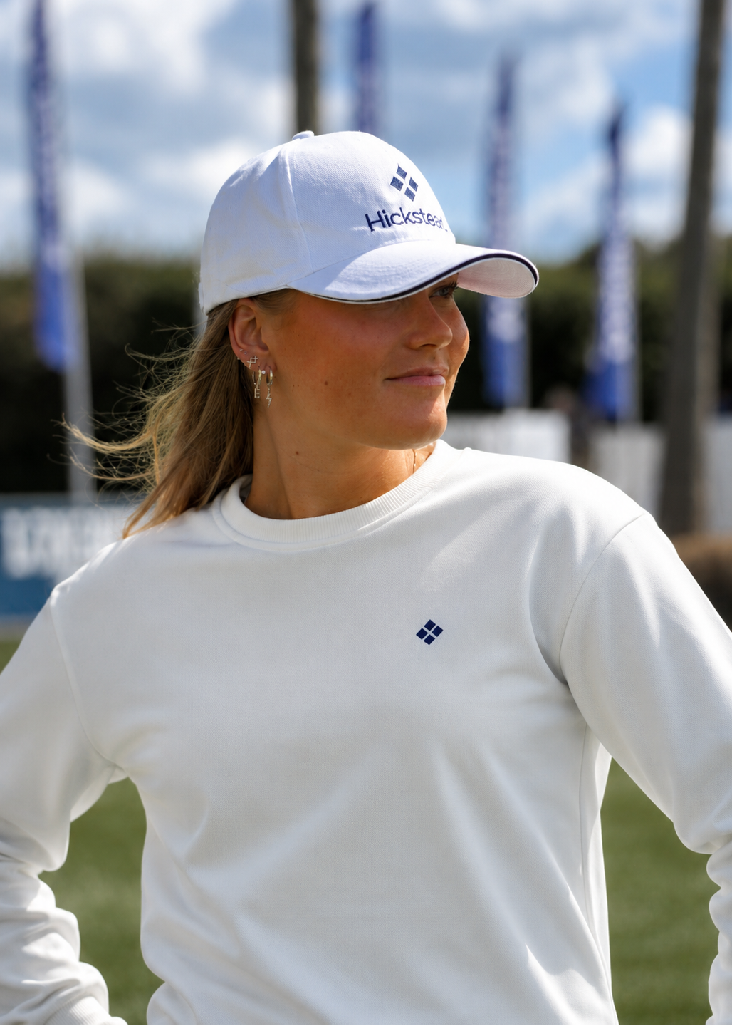 Woman wearing a white cap and long-sleeve shirt with a logo, standing outdoors.