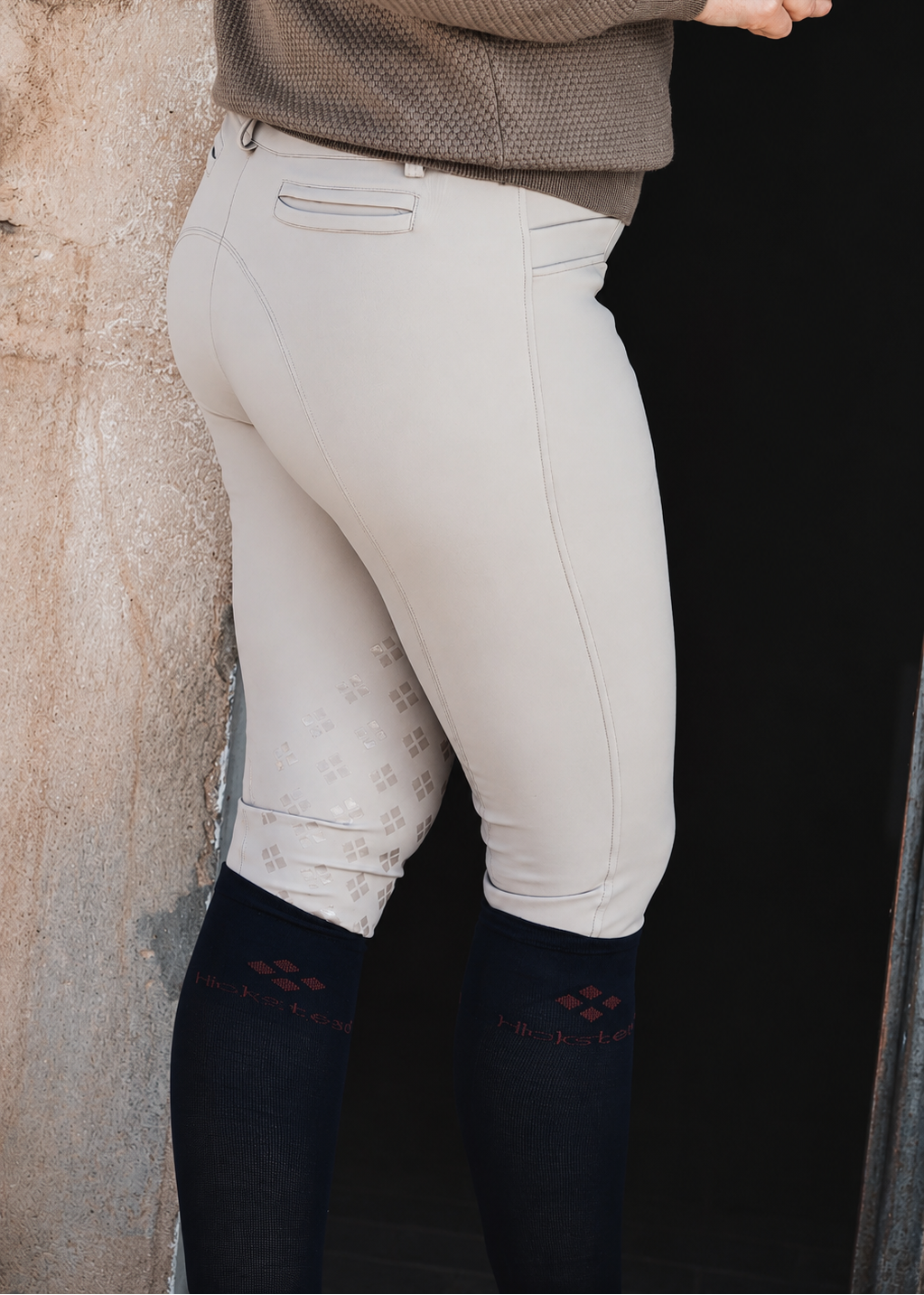 Person wearing beige riding pants against a stone wall.