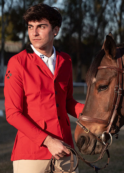 Man in a red jacket standing next to a brown horse outdoors